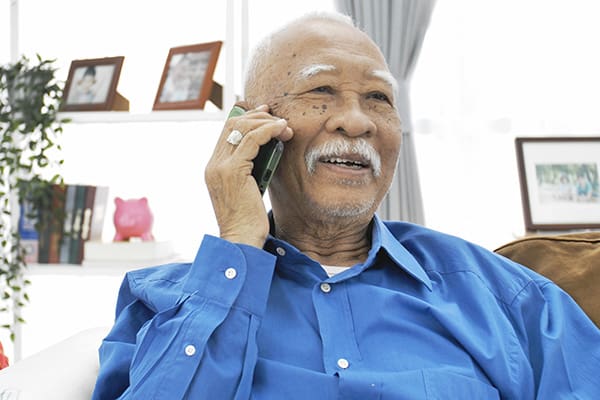 Persona mayor asiática con bigote canoso hablando por un teléfono inteligente.