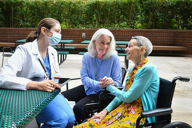 Enfermera y cuidadora visitan a residente de un asilo de ancianos