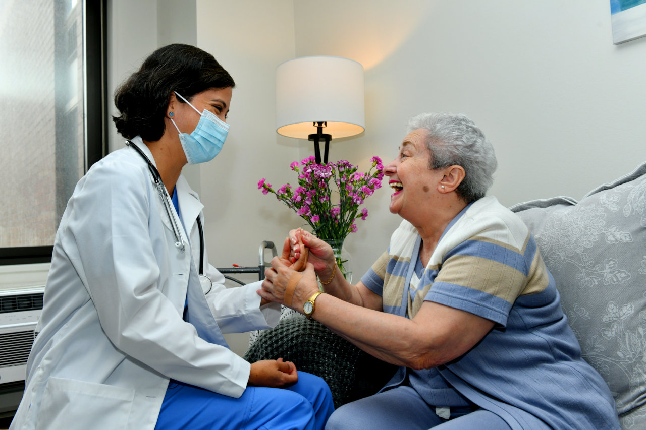 A masked doctor speaks with a smiling patient while they hold hands.