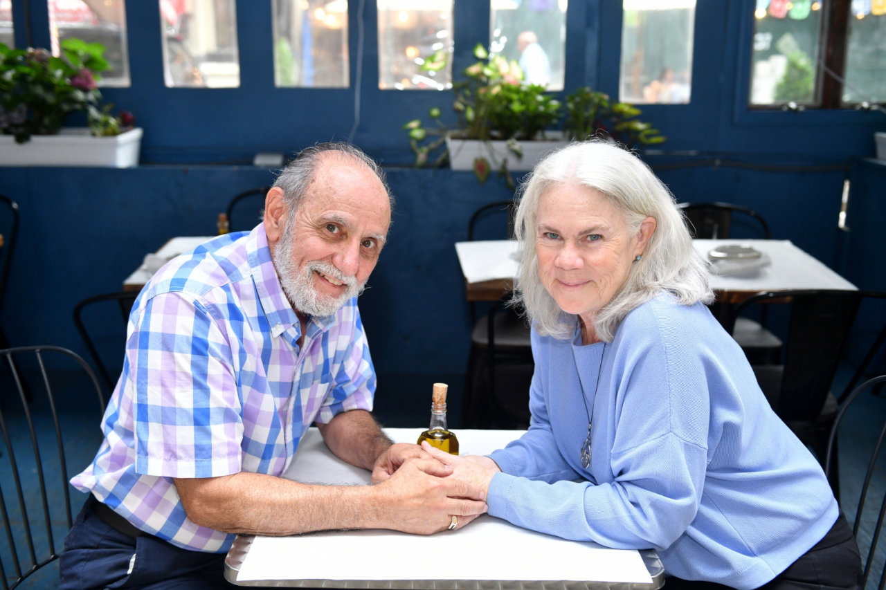 An elderly couple hold hands at a restaurant.